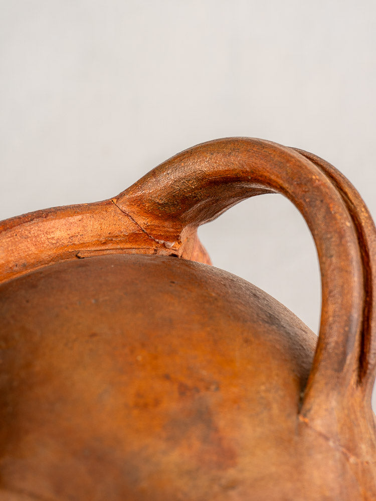 Antique French two-handle glazed earthenware jug with curved handles and rounded body, Southern France, on neutral background.