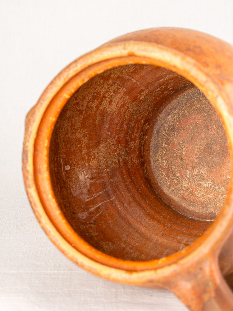 Antique French two-handle 19th-century glazed earthenware jug with rustic texture on a light fabric background.