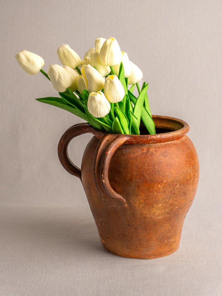 Antique French two-handle glazed earthenware jug with white tulips, Southern France, set on light gray background.