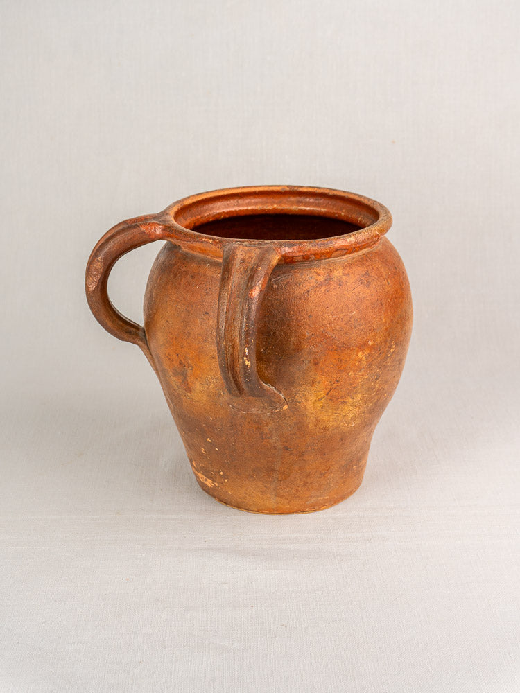 Antique French two-handle glazed earthenware jug with rustic, weathered finish on a neutral background.