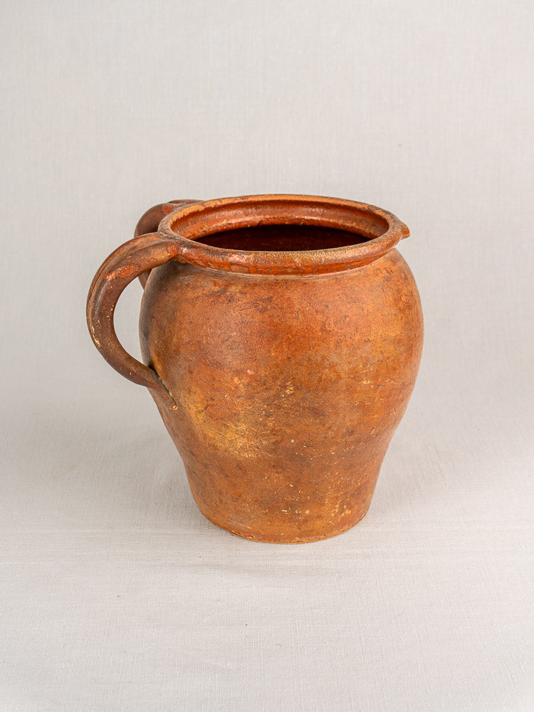 Antique 19th-century French two-handle glazed earthenware jug with rustic finish, set against a plain light background.