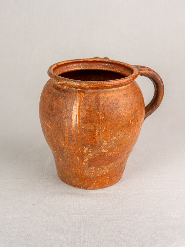Antique French two-handle glazed earthenware jug with textured surface on a light fabric background. 19th century Southern France.