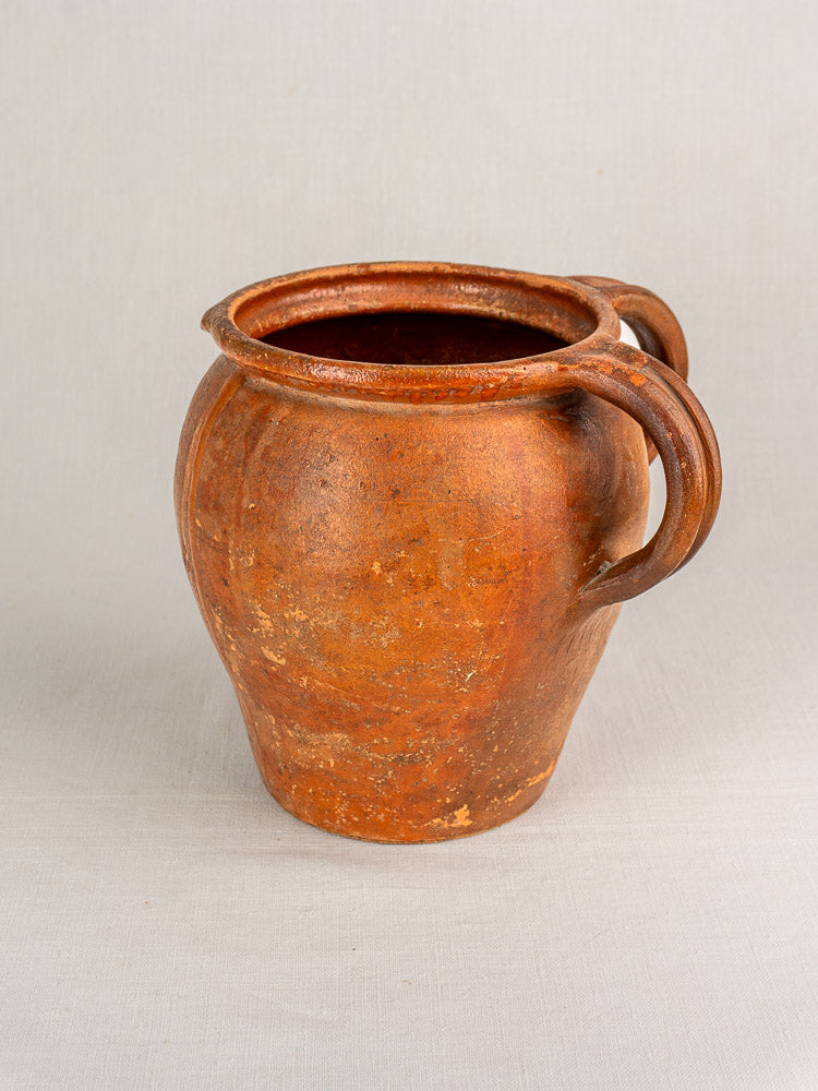 Antique French two-handle glazed earthenware jug from 19th-century Southern France on light grey cloth.
