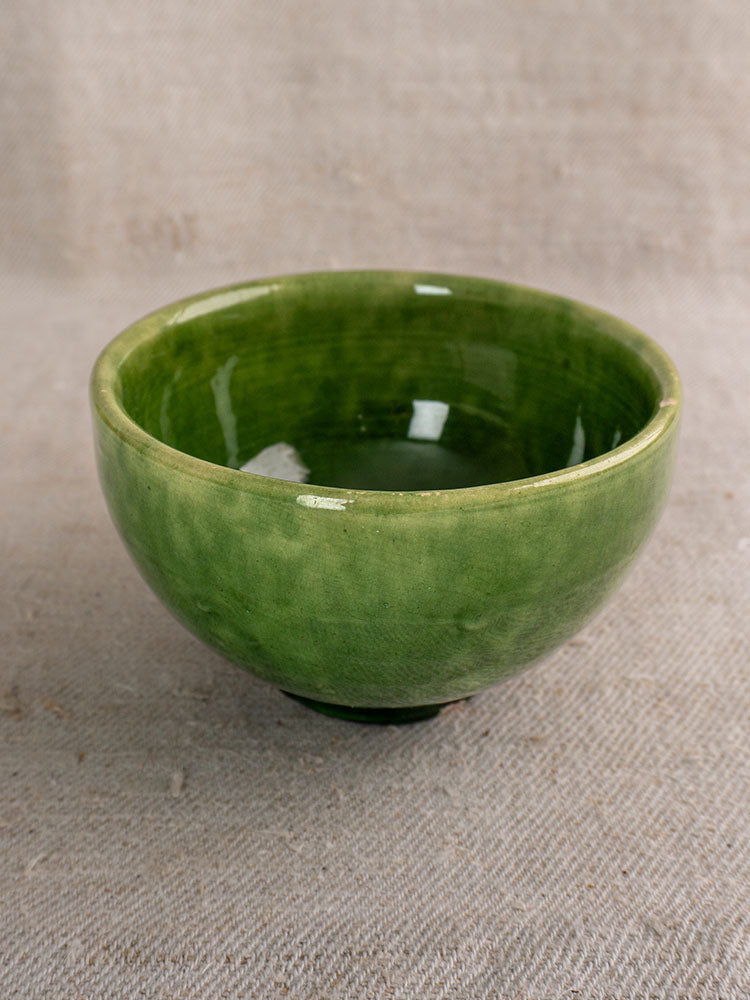 Set of antique French green glazed earthenware bowls with glossy finish on textured beige fabric.