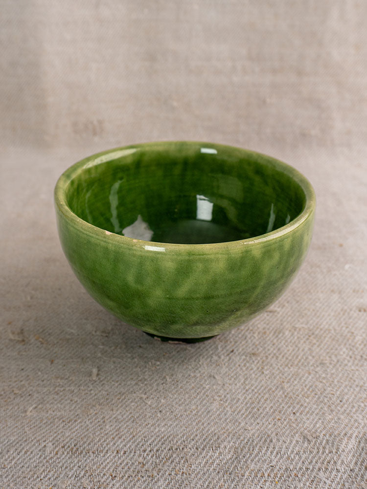 Antique French green glazed earthenware bowls with glossy finish displayed on textured beige fabric.