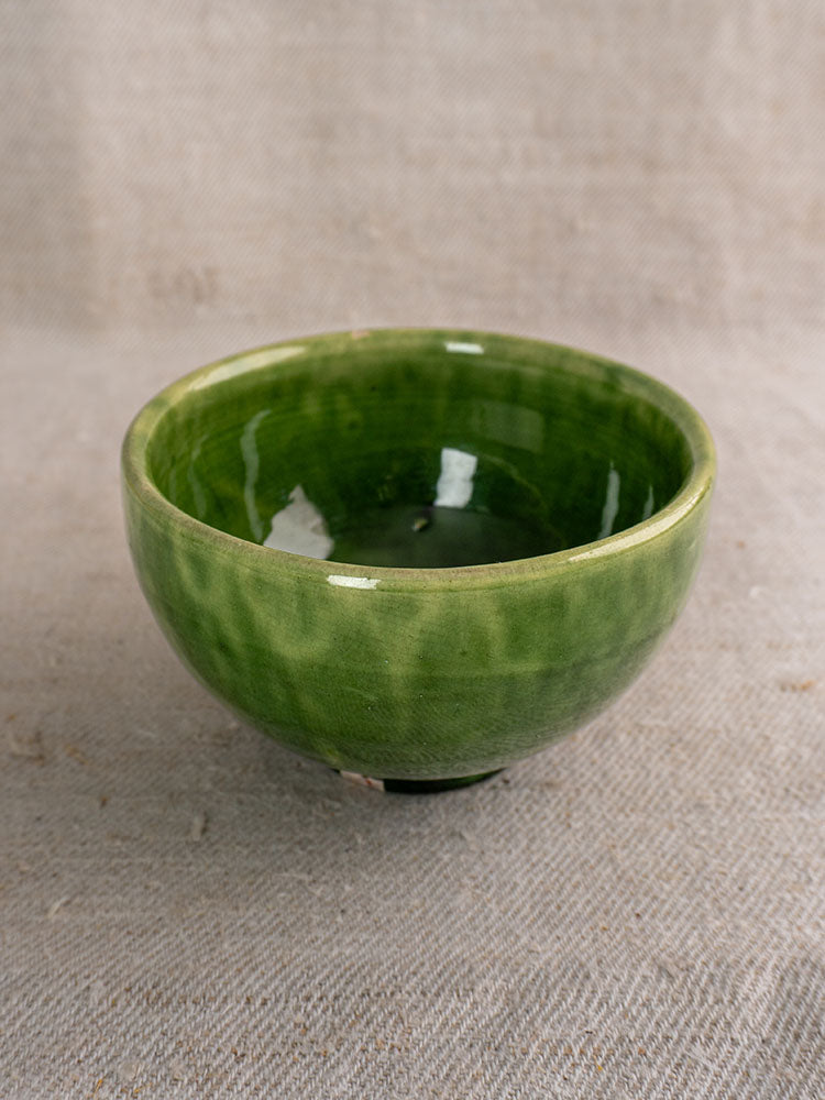 Set of antique French green glazed earthenware bowls with glossy finish on textured beige fabric.