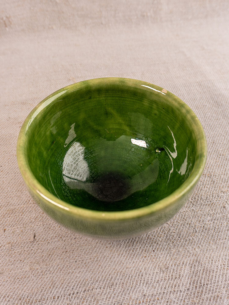 Set of antique French green glazed earthenware bowls with glossy finish on a textured fabric background.