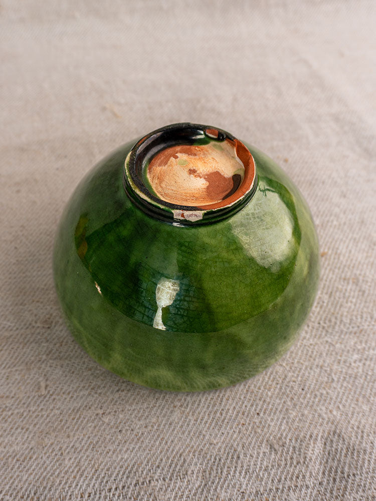 Set of antique French green glazed earthenware bowls, upside down, showing unglazed reddish-brown clay bases on beige fabric.