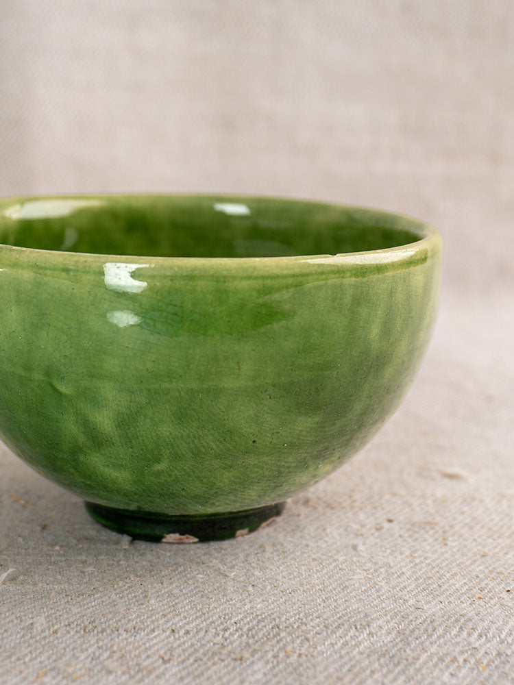 Antique French green glazed earthenware bowl with glossy finish, partial view on beige textured fabric backdrop.