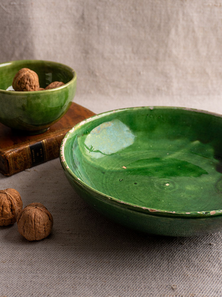 Antique French green glazed earthenware bowls, one large and one small, with walnuts on beige textured fabric.