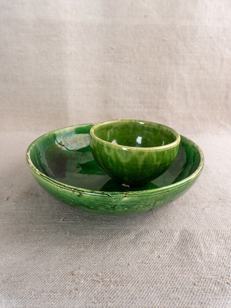 Pair of antique French green-glazed earthenware bowls, large and small, stacked on textured beige fabric backdrop.