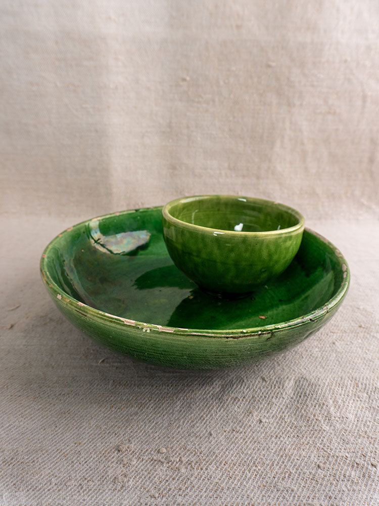 Antique French green glazed earthenware bowls, small nested inside large, on textured beige fabric.