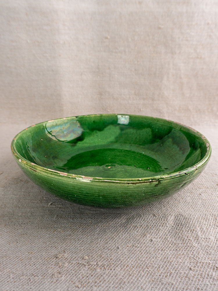 Set of antique French green glazed earthenware bowls with rustic edges on textured beige fabric.