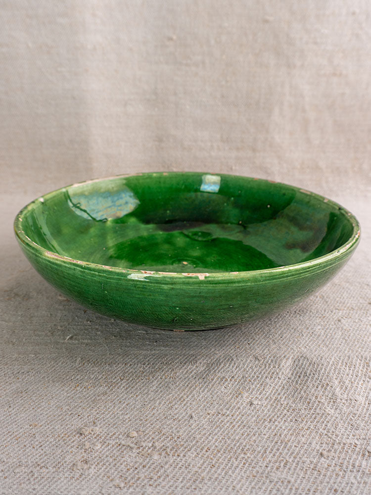 Antique French green glazed earthenware bowls with glossy finish, arranged on textured beige fabric for Provence kitchen decor.