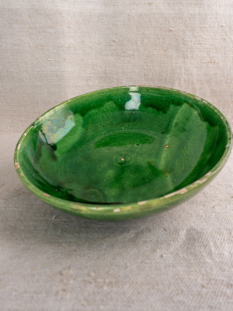 Antique French green glazed earthenware bowls with glossy finish and rustic imperfections on beige textured fabric.
