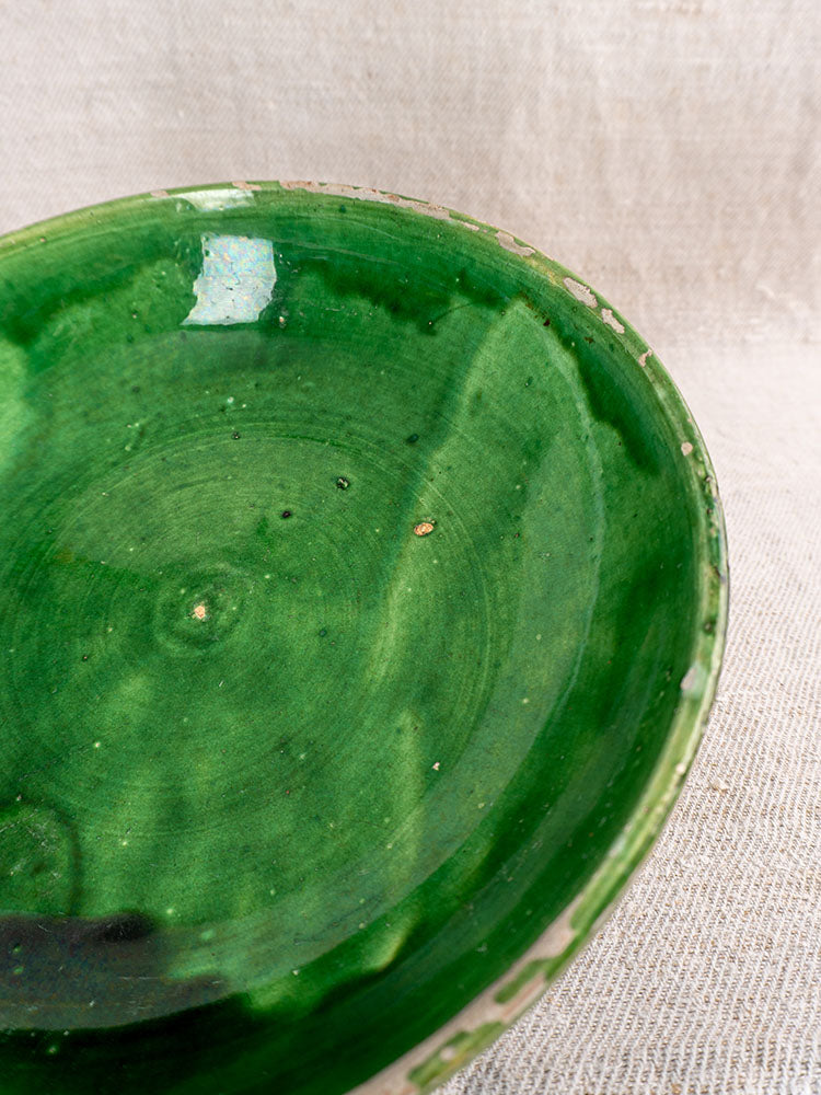 Antique French green glazed earthenware bowls with glossy finish and rustic edges on textured beige fabric.
