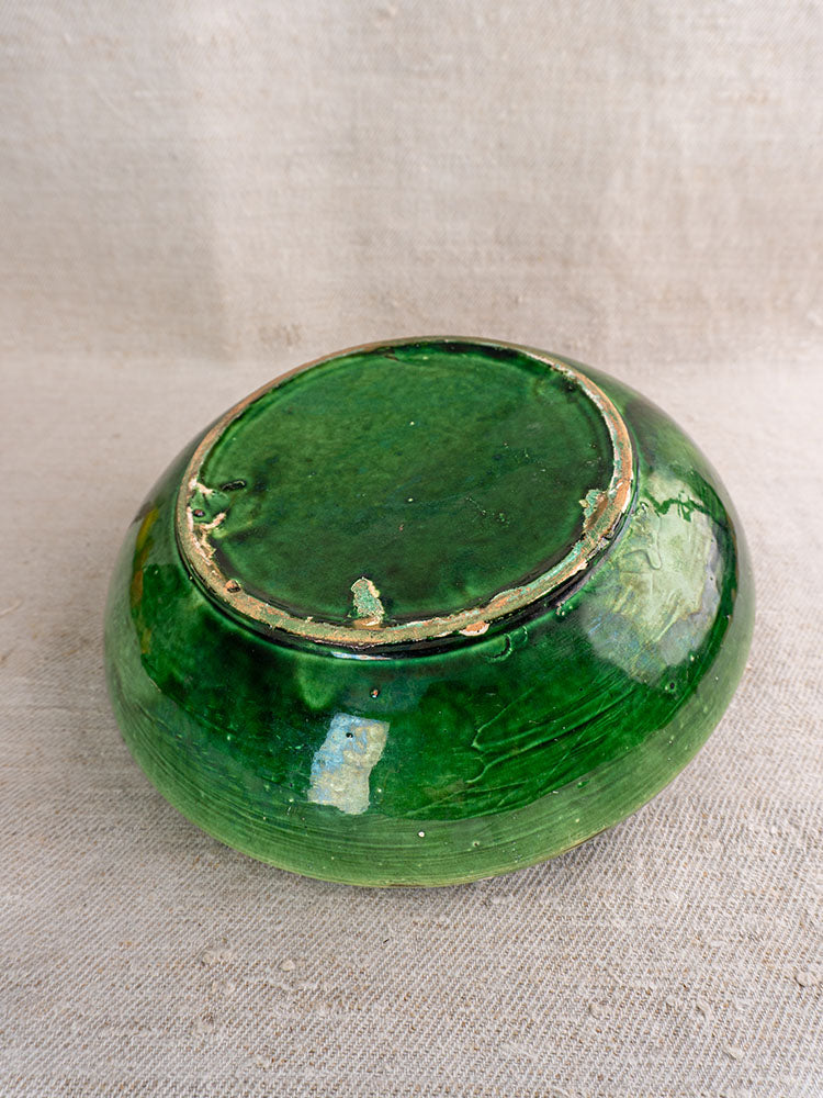 Antique French green glazed earthenware bowl upside down, displaying unglazed, worn rim and base on beige textured fabric.
