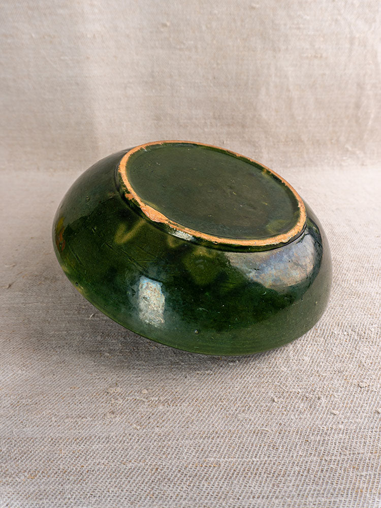 Pair of green glazed Provençal serving bowls upside down, revealing unglazed bases on textured light beige fabric.