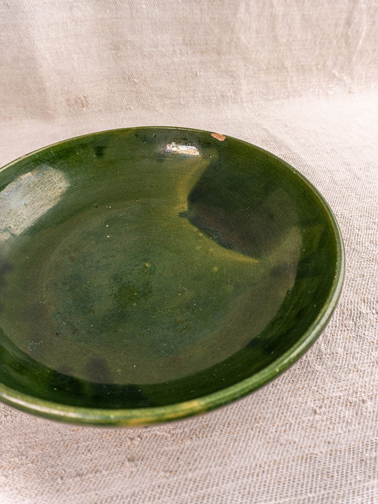Pair of vintage green glazed Provençal serving bowls with glossy finish and small rim chip on beige textured fabric.