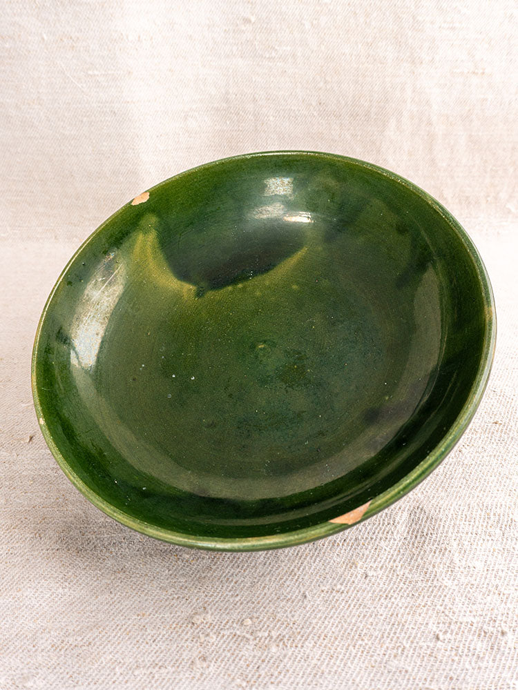 Pair of vintage French Provençal serving bowls with deep green glaze and rim chips on textured beige fabric.