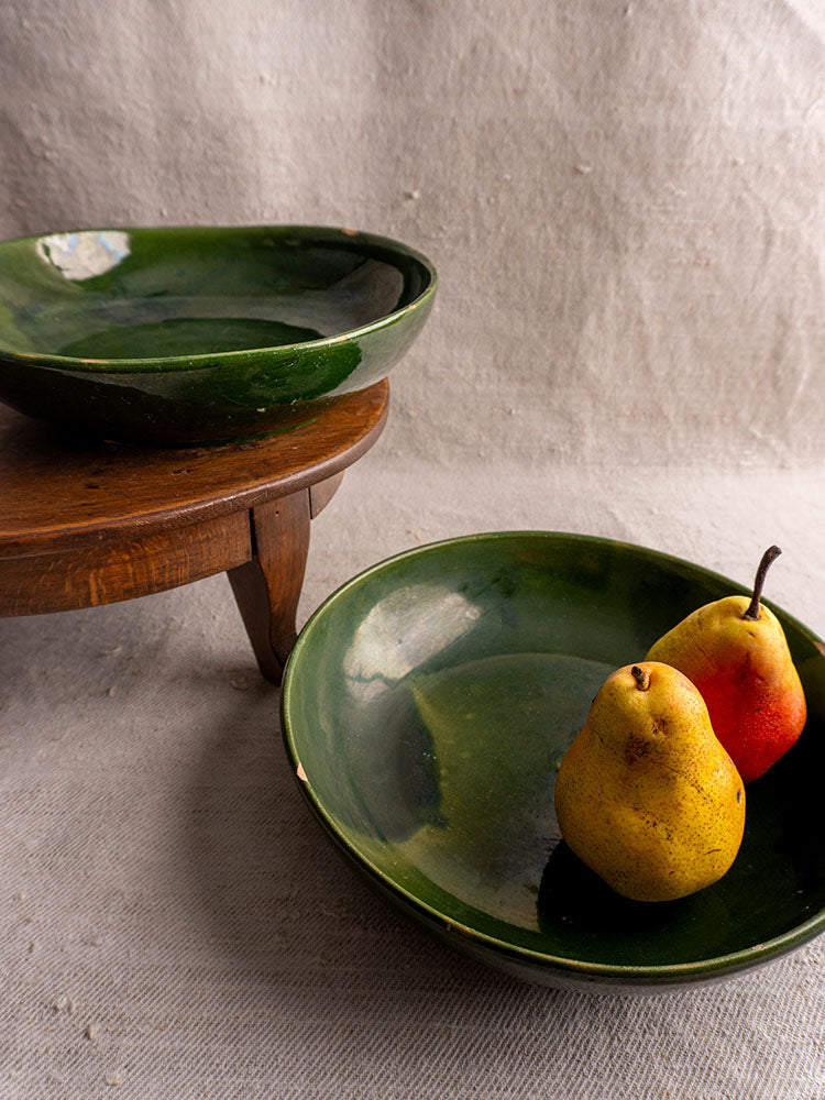 Green glazed Provençal vintage French pottery serving bowls stacked on textured beige fabric background.