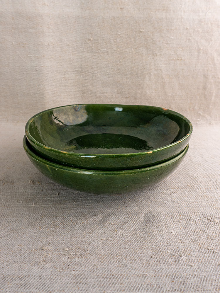 Green glazed Provençal vintage French pottery serving bowls stacked on textured beige fabric background.