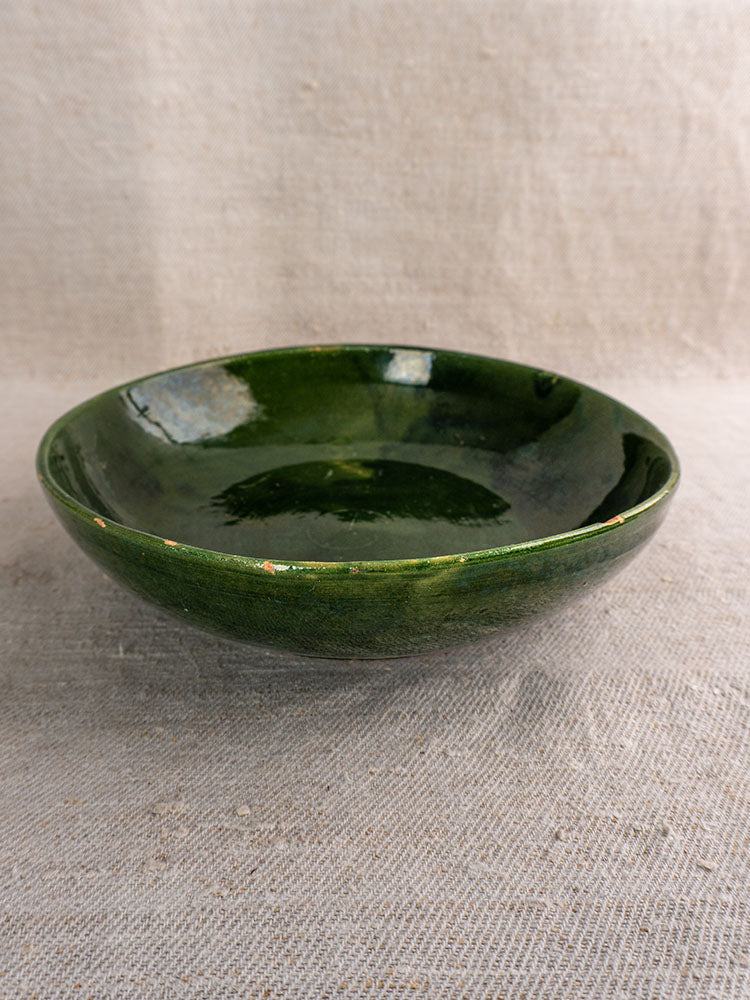 Pair of green glazed Provençal serving bowls from vintage French pottery on textured beige fabric, neutral backdrop.