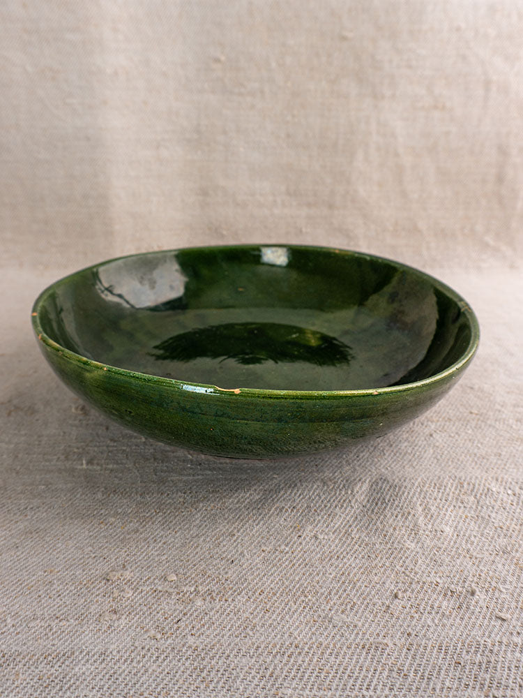 Pair of green glazed Provençal serving bowls with glossy finish on textured beige fabric background. Vintage French pottery.