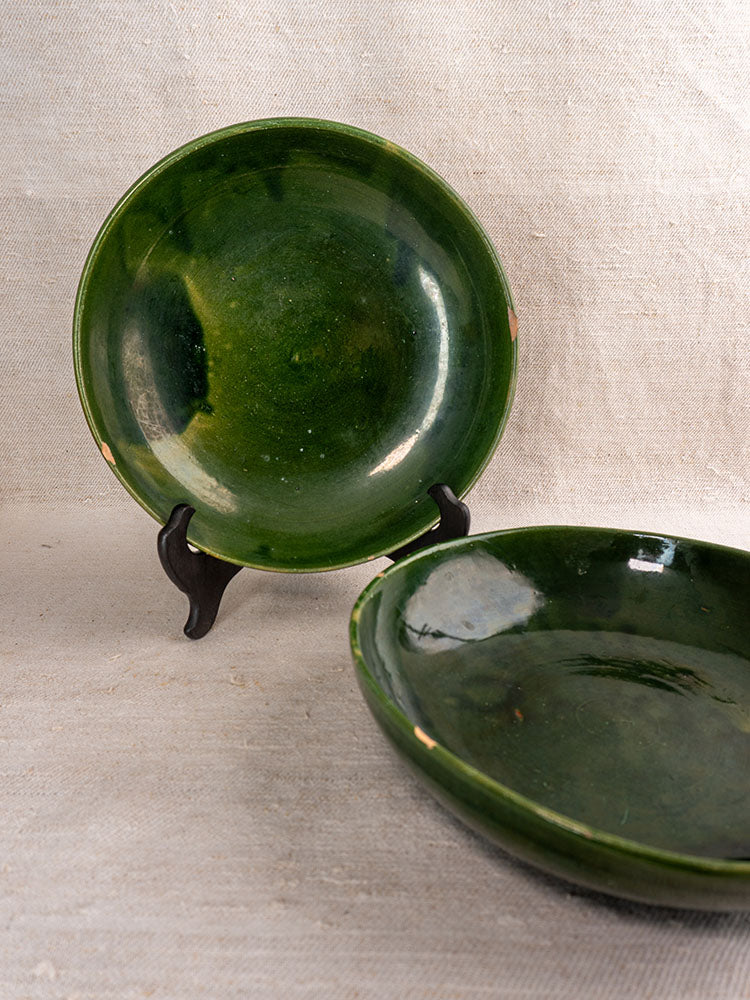 Pair of vintage green glazed French pottery serving bowls with glossy finish on neutral textured fabric background.