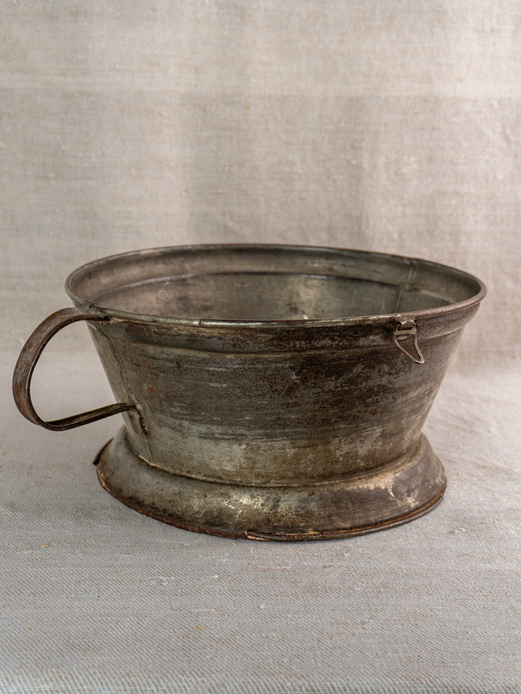 Antique French tinned sheet iron passoire with rosette base and handle on light gray fabric.