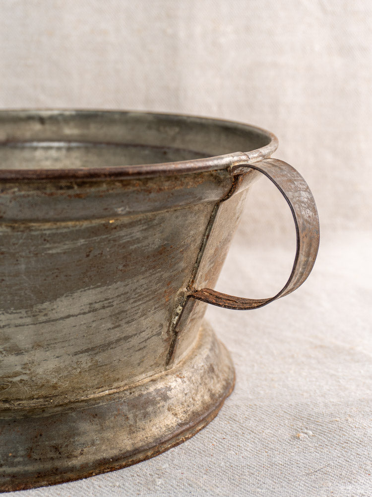 Antique French passoire in tinned sheet iron with pierced rosette base, on light fabric.