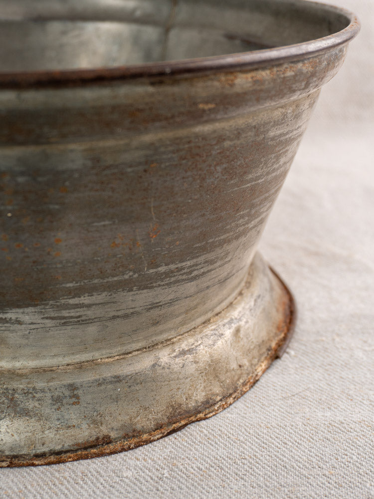 Antique French passoire in tinned sheet iron with pierced rosette base on textured fabric surface.