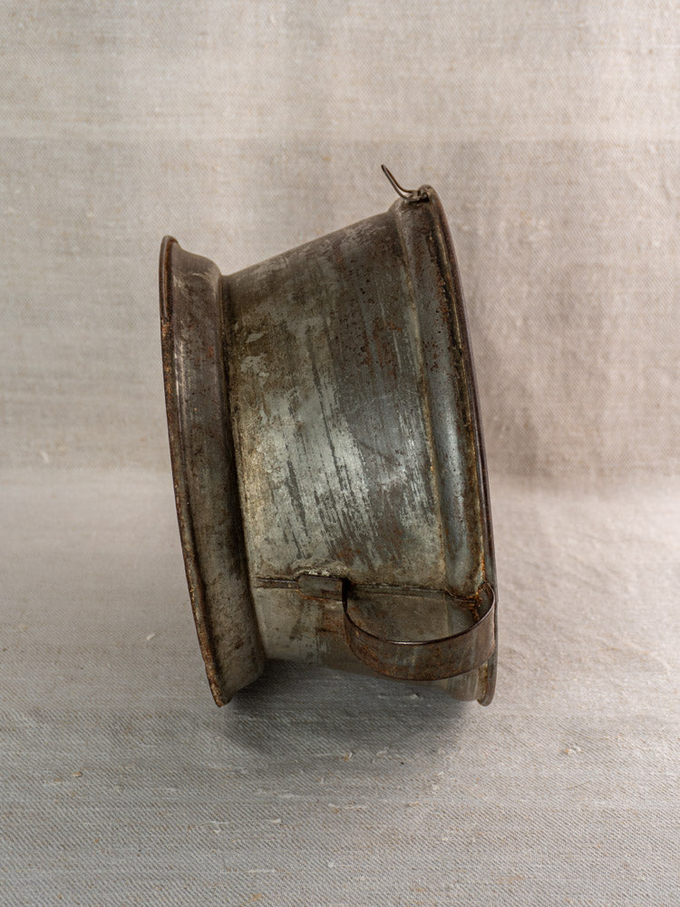 Antique French tinned sheet iron passoire with pierced rosette base and sturdy handle on neutral fabric.