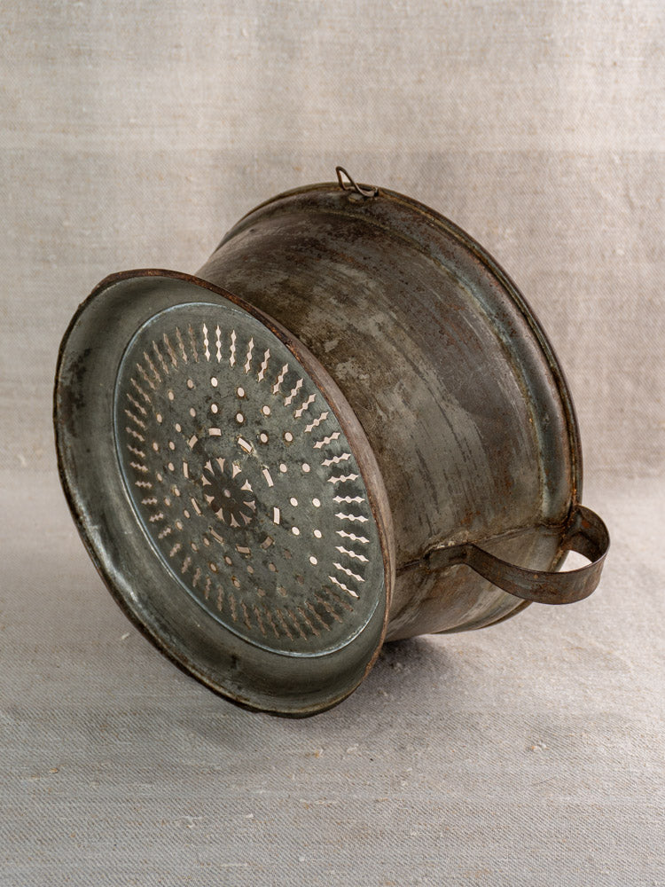 Antique French passoire in tinned sheet iron, pierced rosette base, timeworn patina on neutral fabric.