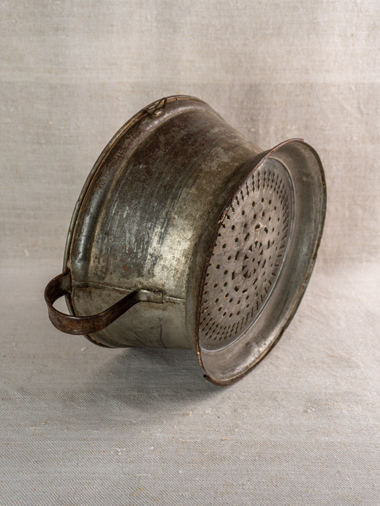 Antique French tinned sheet iron passoire with pierced rosette base and handle on neutral fabric.