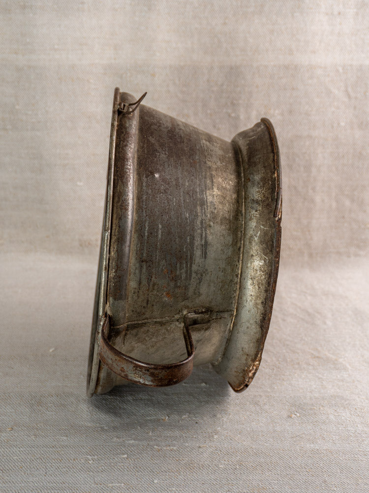 Antique French tinned sheet iron passoire with pierced rosette base, displayed on textured beige background.