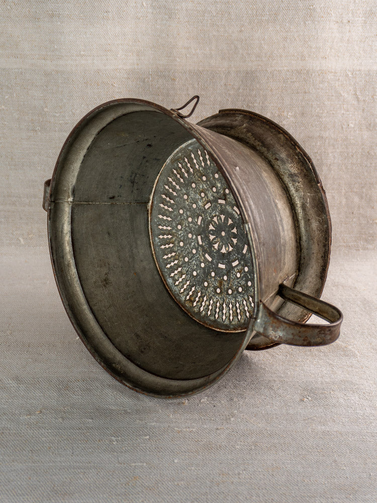 Antique French passoire in tinned sheet iron, pierced rosette base shown against neutral fabric.
