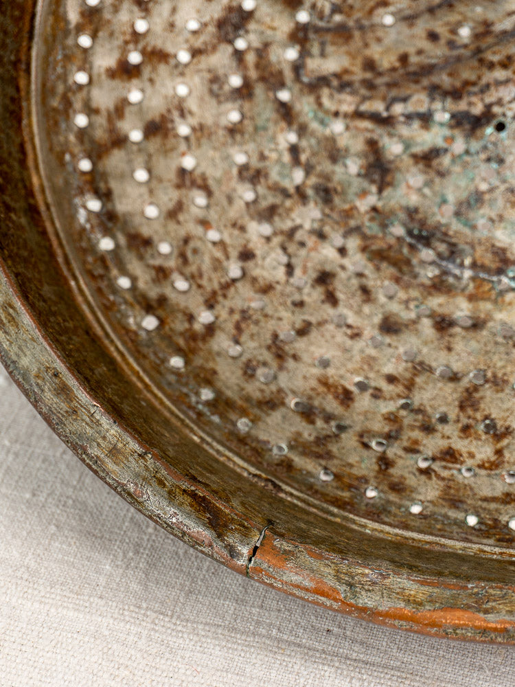 Antique French copper colander with small drain holes and outer rim crack on beige textured fabric.
