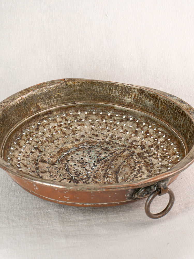 Antique French copper colander with hammered finish, perforated base, and metal ring handle on a neutral surface.