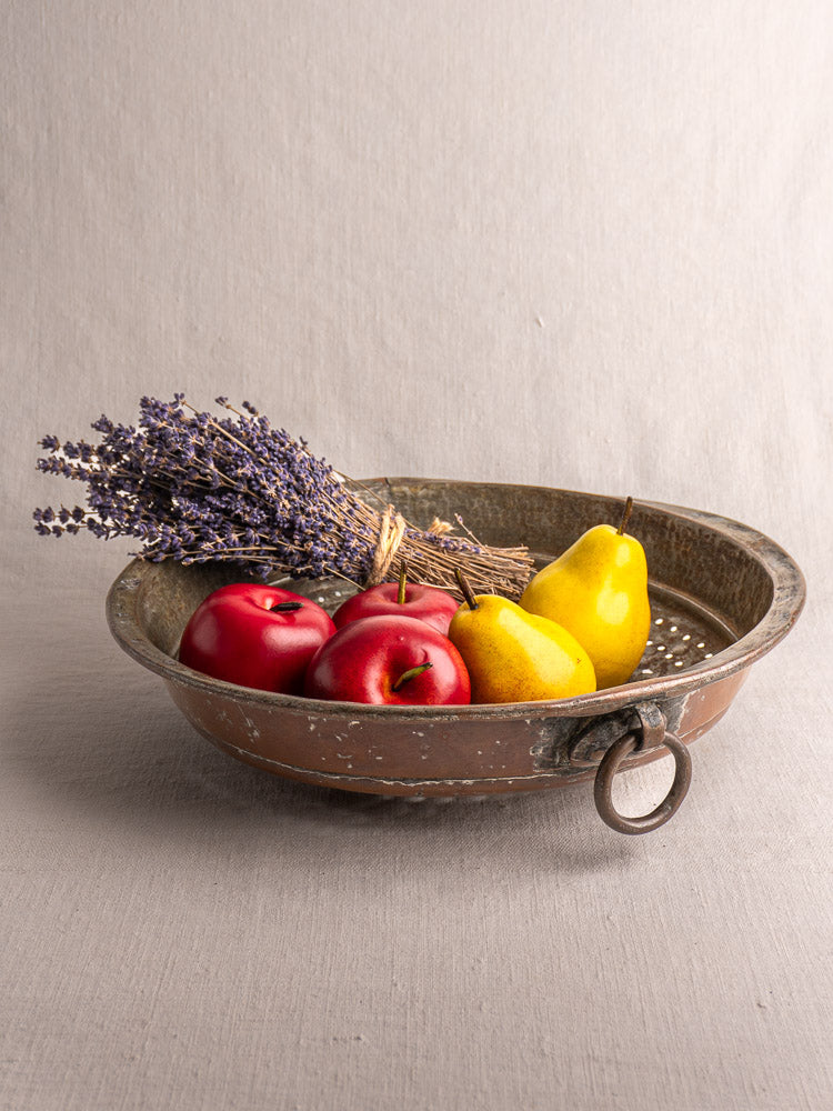 Antique French copper colander with a large ring handle, displayed upside down on a light surface.