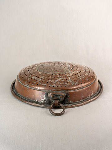 Antique French copper colander with a large ring handle, displayed upside down on a light surface.