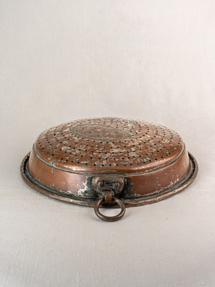 Antique French copper colander with a large ring handle, displayed upside down on a light surface.