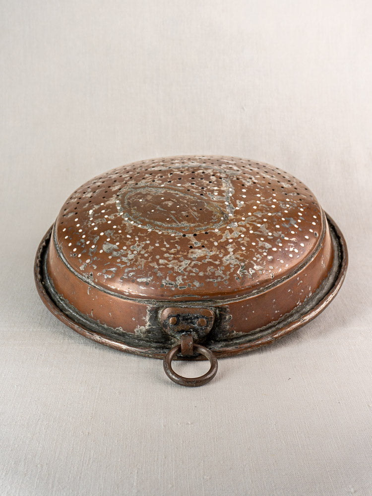 Antique French copper colander with hand-tinned interior and aged patina on a light fabric background.