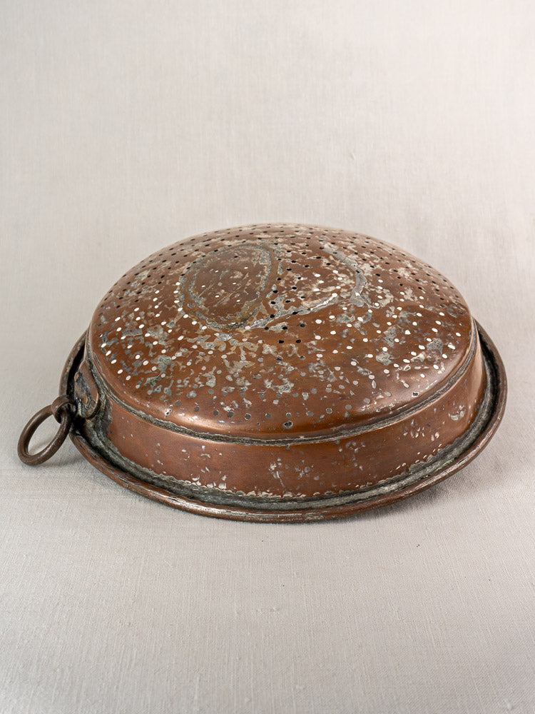 Antique French copper colander, 19th century, hand-tinned with hammered round design and handle on light fabric surface.
