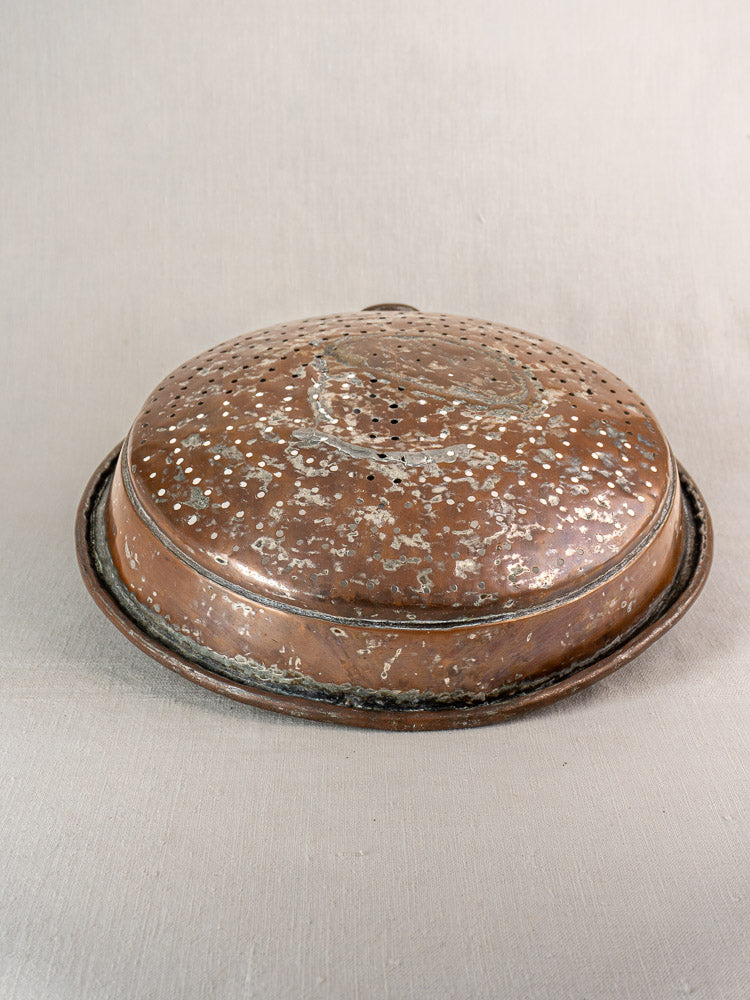 Antique French copper colander with hand-tinned interior and aged patina, small perforations, on a neutral background.