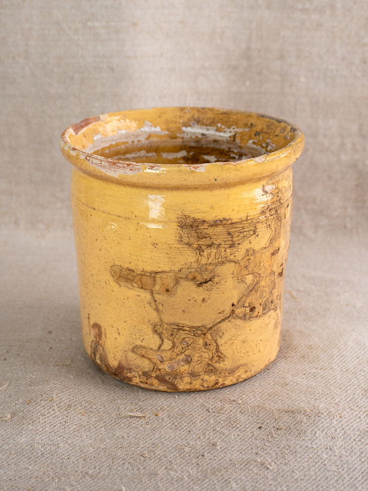Antique French yellow glazed earthenware confit pot with rustic wide rim and brown markings on beige fabric.