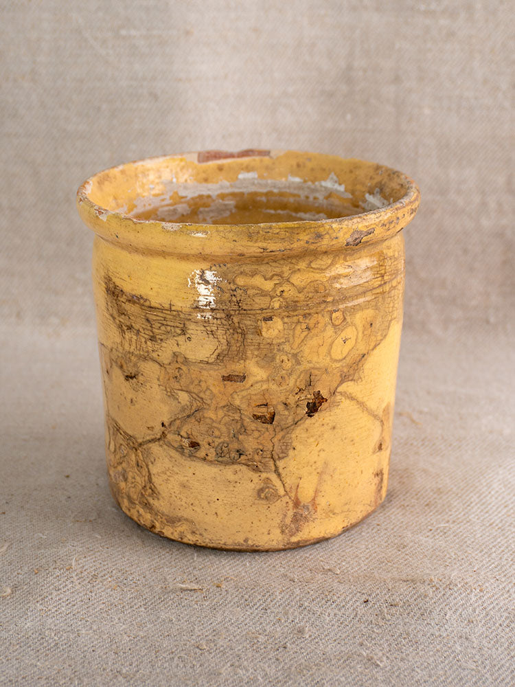 Antique French confit pot with yellow glaze, wide rim, and textured surface on neutral coarse fabric.