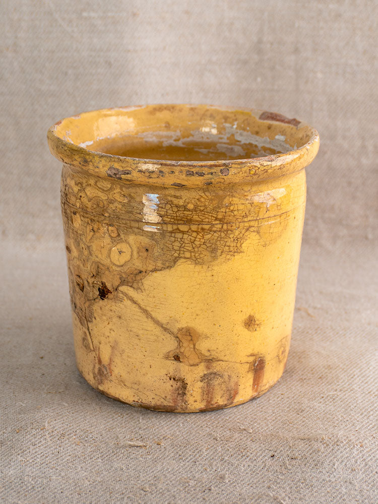 Antique French confit pot with crackled yellow glaze and wide rim, shown on beige textured fabric.