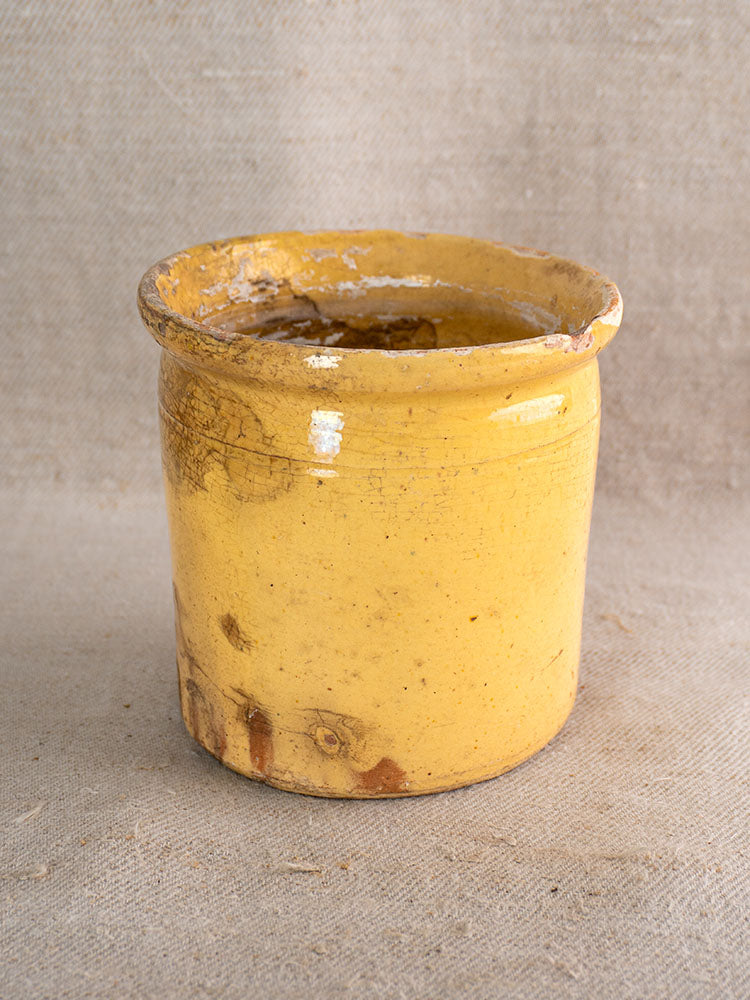 Antique French yellow-glazed Provençal confit pot with aged chips, displayed on textured beige fabric.