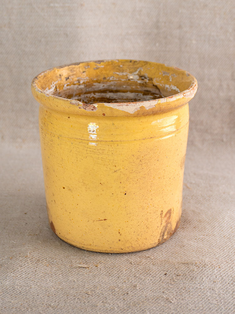 Antique French confit pot with rustic yellow glaze, wide mouth, and weathered edges showing Provençal patina.